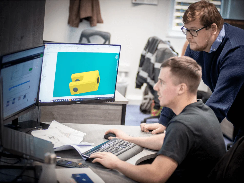 Engineer sat at desk receiving help on CAD for his career in Offshore Engineering